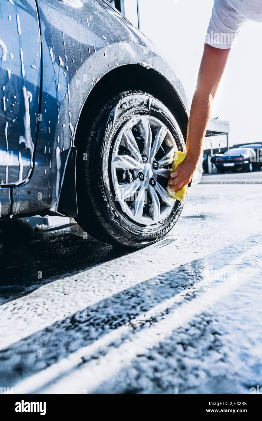 A man washes his car with foam at a selfservice car wash, wheels and tires closeup Stock Photo