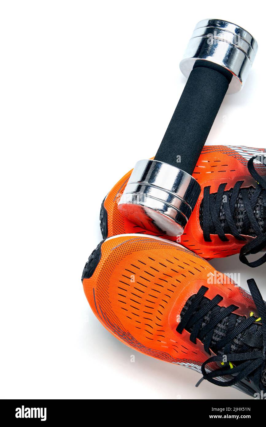 Metallic heavy dumbbell dropped on leg in orange sneaker isolated on