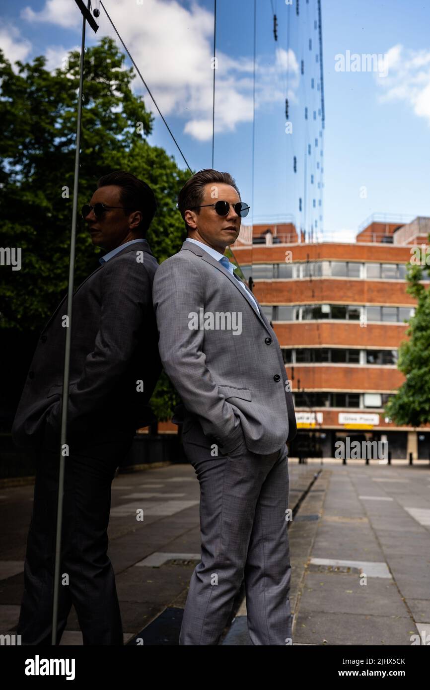 A handsome businessman in a grey suit and sunglasses in an urban city environment Stock Photo