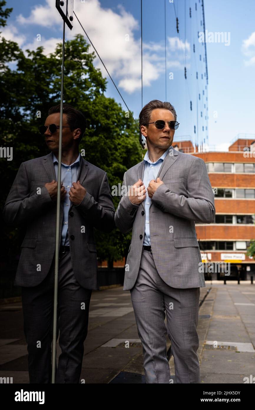 A handsome businessman in a grey suit and sunglasses in an urban city environment Stock Photo