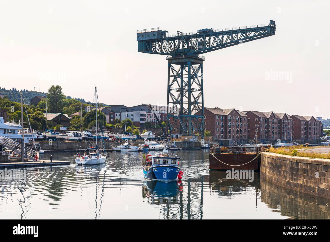 James Watt marina, with berthed yachts and the shipbuilding cantilever crane in the distance, local fishing boat approaching the pier, Port Glasgow. Stock Photo