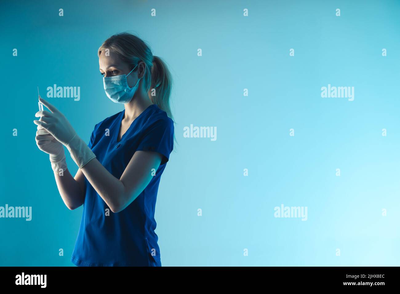 young lady nurse with a protective mask holiding a vaccination syringe - light blue background closeup. High quality photo Stock Photo