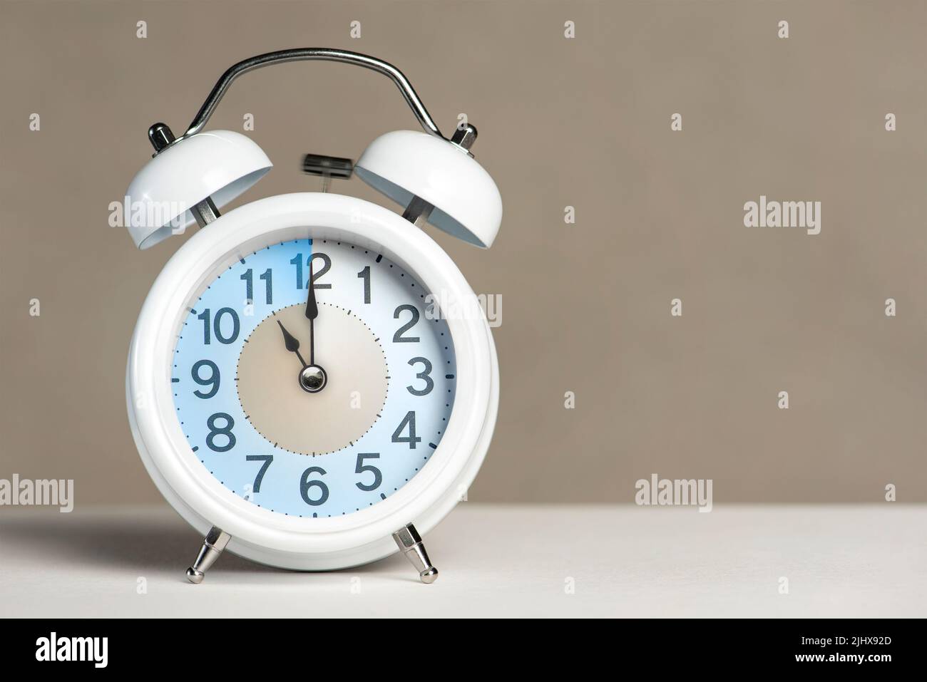 Eleven o'clock on the alarm. A white alarm clock is on a white table. The clock hand points to 11 o'clock. Time to change to summer or winter time Stock Photo