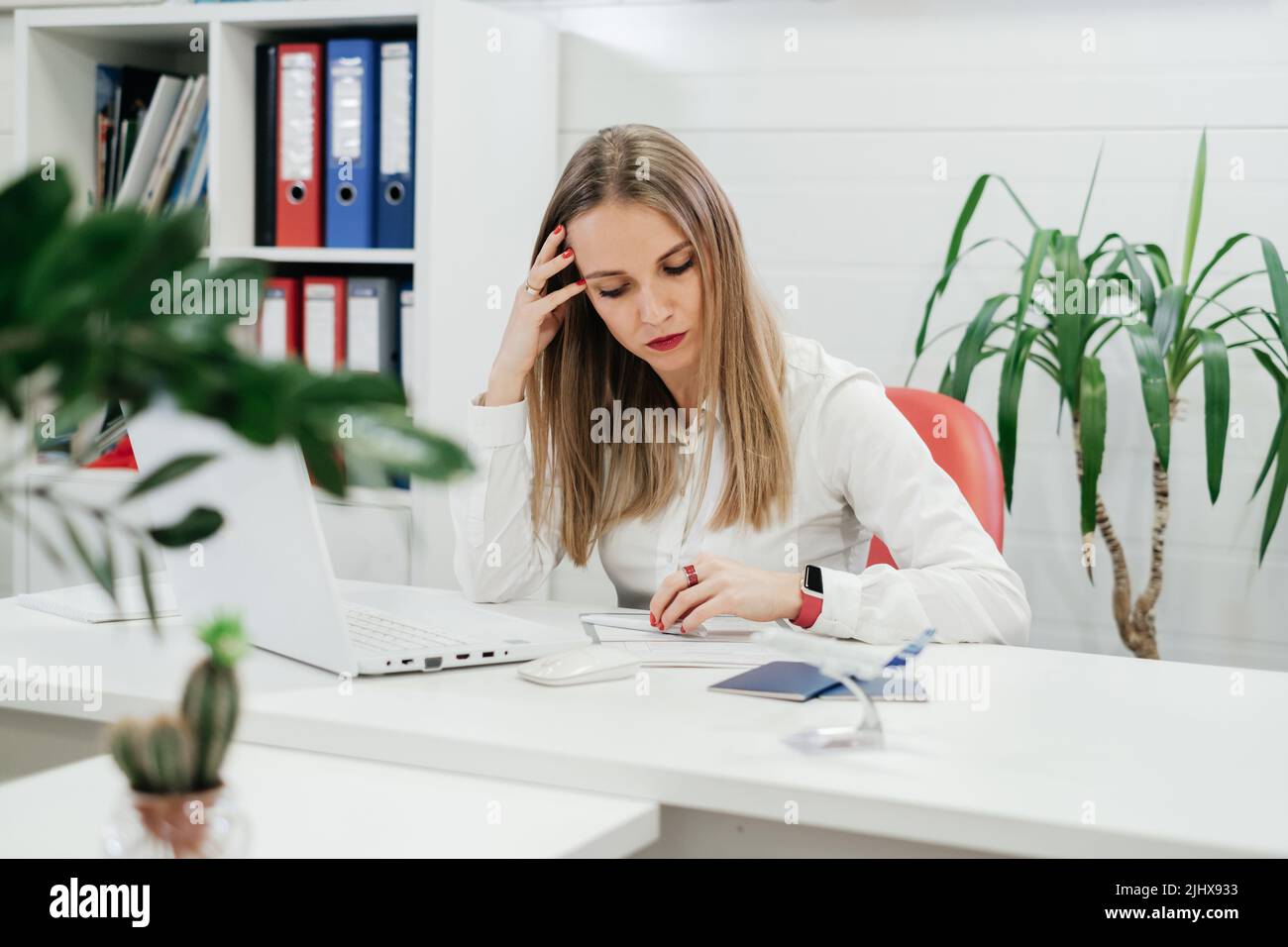 Tired businesswoman using laptop and smartphone for communication and work on-line in modern environment with plants. Travel agency hard time Stock Photo