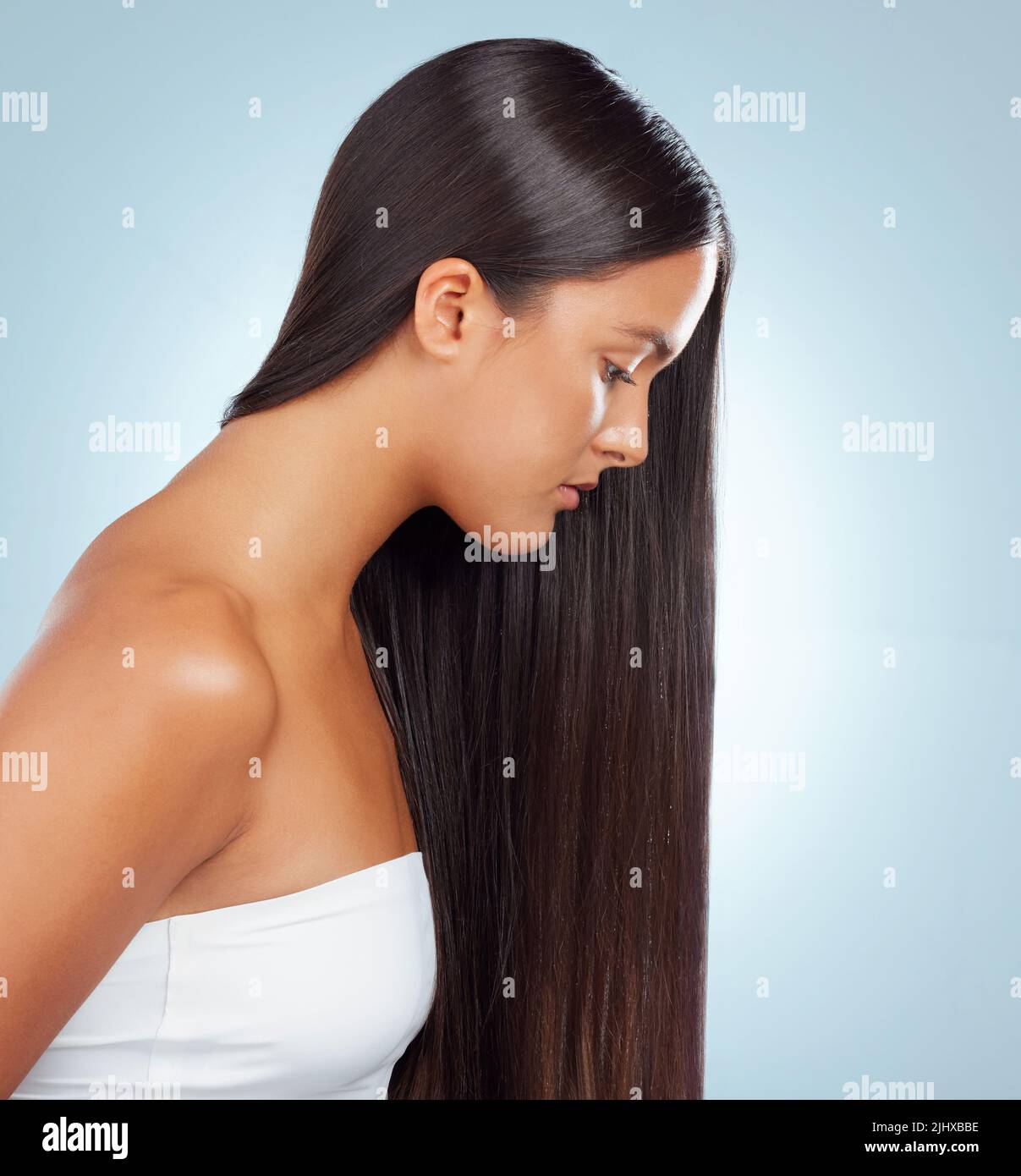 A hispanic brunette woman with long lush beautiful hair posing and looking serious against a grey studio background. Mixed race female standing Stock Photo