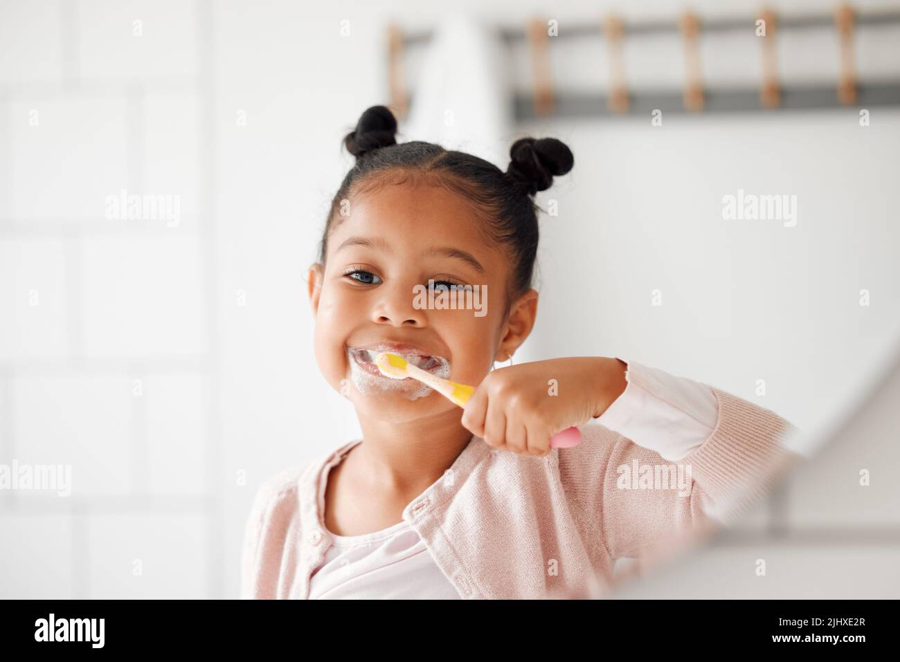 One mixed race adorable little girl brushing her teeth in a bathroom at home. A happy Hispanic child with healthy daily habits to prevent cavities and Stock Photo