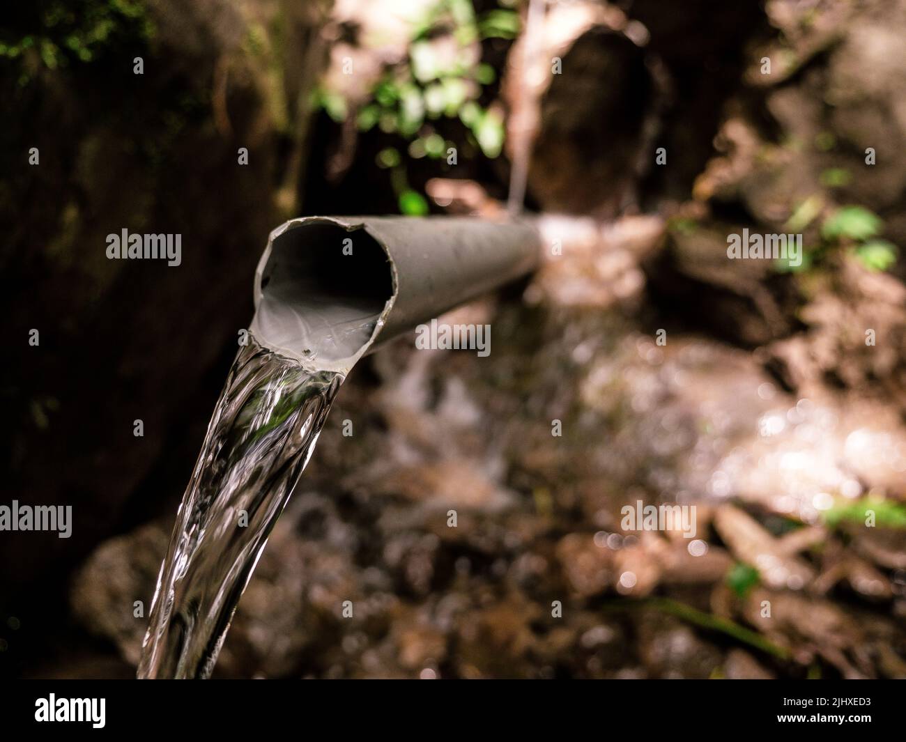 Clear stream water pouring from broken plastic pipe Stock Photo