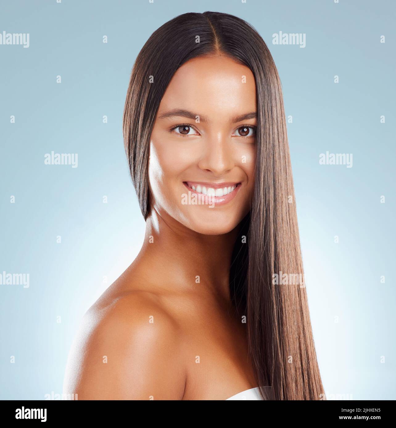 Portrait of a hispanic brunette woman with long lush beautiful hair smiling and posing against a grey studio background. Mixed race female standing Stock Photo