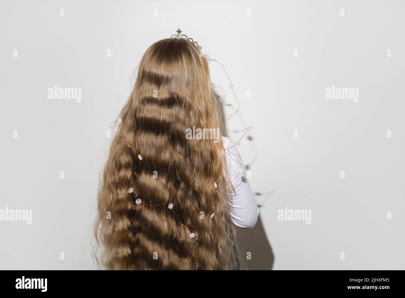 Back view of child girl with long blond wavy flowing hair and crown with a garland of snowflakes on her head. Child celebrates Christmas and Happy Birthday. Copy space for text. Soft selective focus Stock Photo