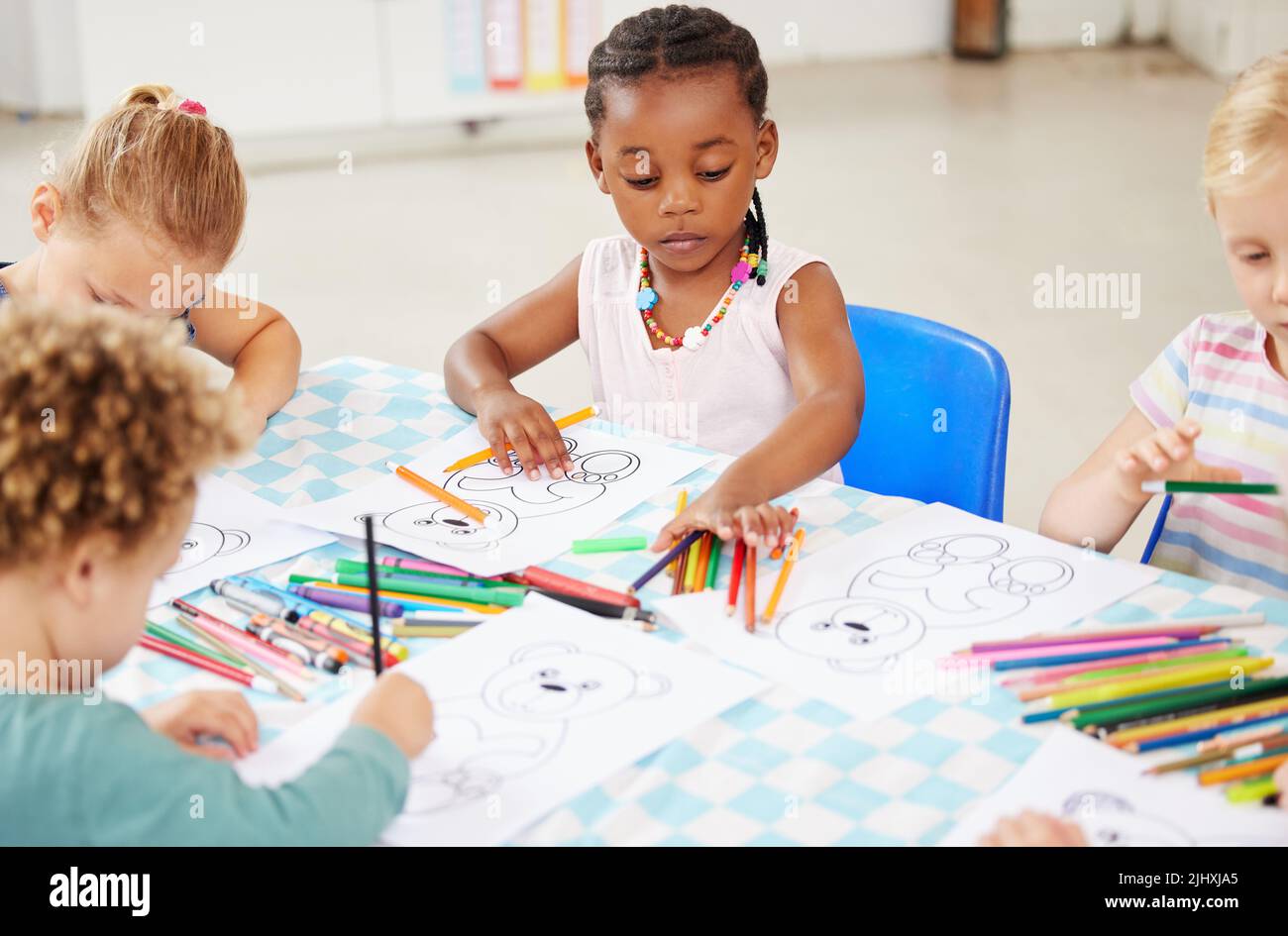 Diverse group of children sitting at a table and colouring at pre-school or kindergarten. Group of kids with colourful pencils and pictures Stock Photo