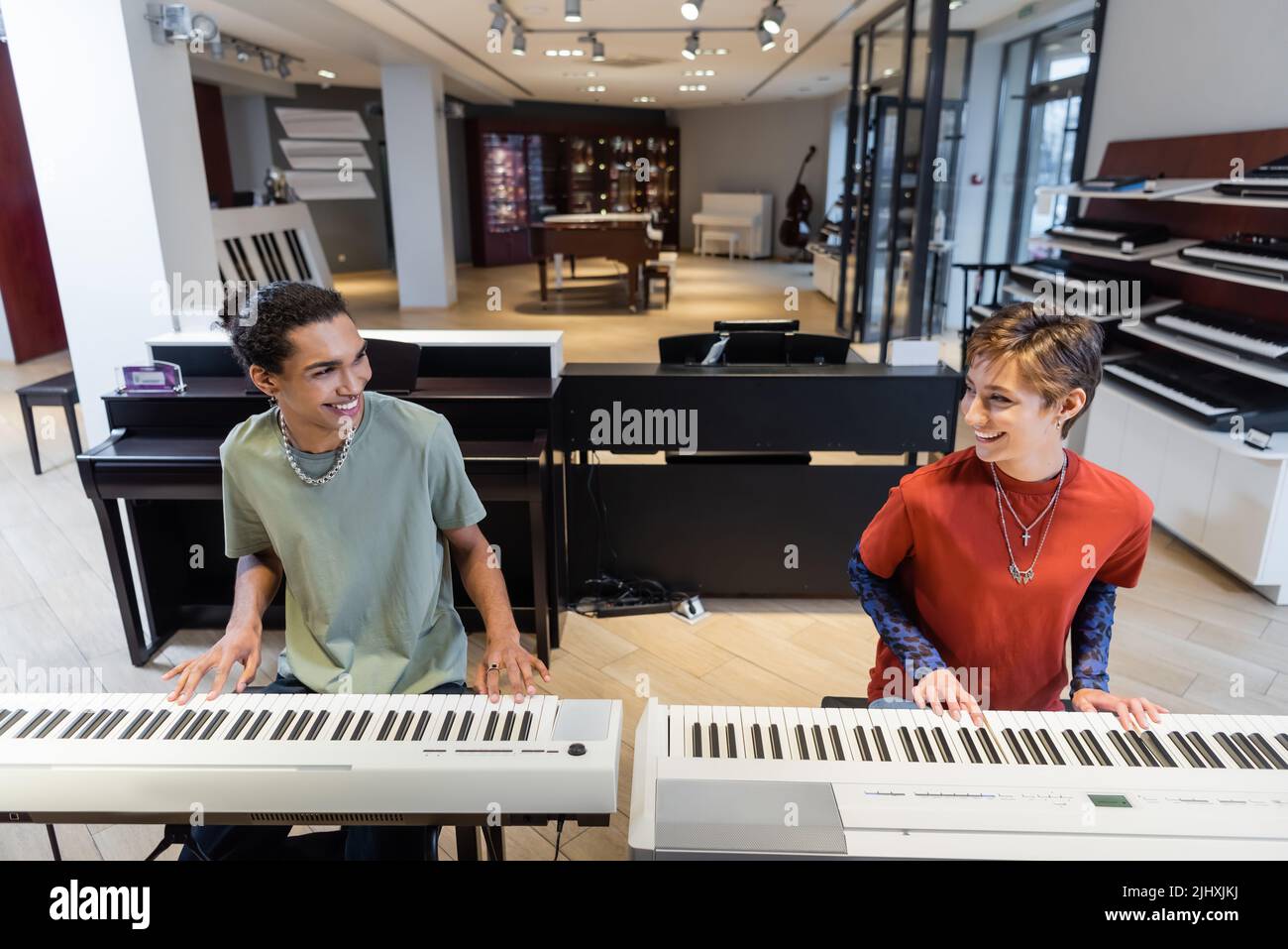 Positive multiethnic couple playing synthesizers in music shop Stock Photo