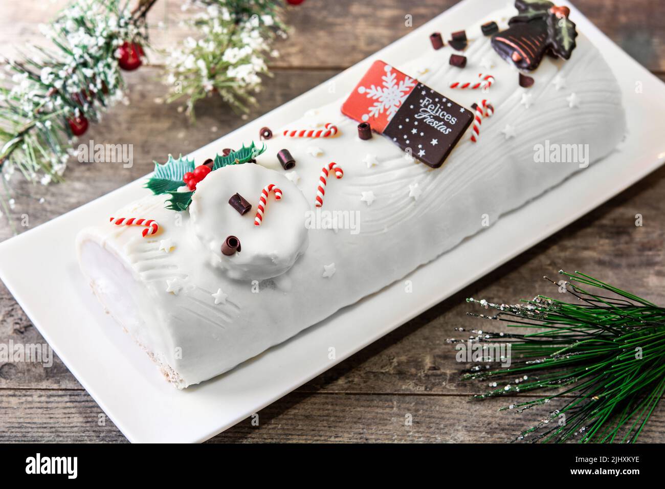 White chocolate yule log cake with ornament on wooden table. Stock Photo