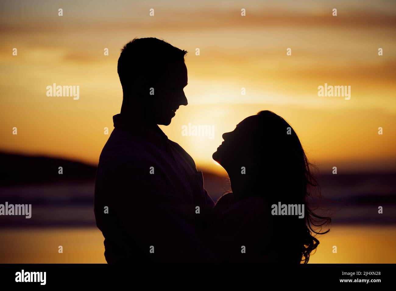 Silhouette couple enjoying romantic moment standing face to face looking into eyes at sunset. Unknown boyfriend and girlfriend feeling in love while Stock Photo