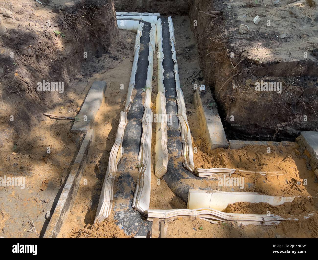 Laying a water pipe in a trench in the ground with insulation. Stock Photo