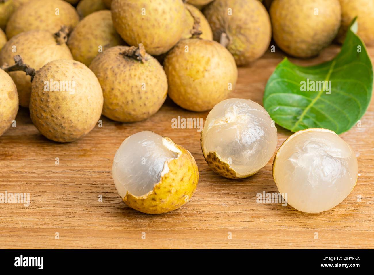 Closeup view of peeled longan and pile of the whole with green leaf on wooden table. Stock Photo