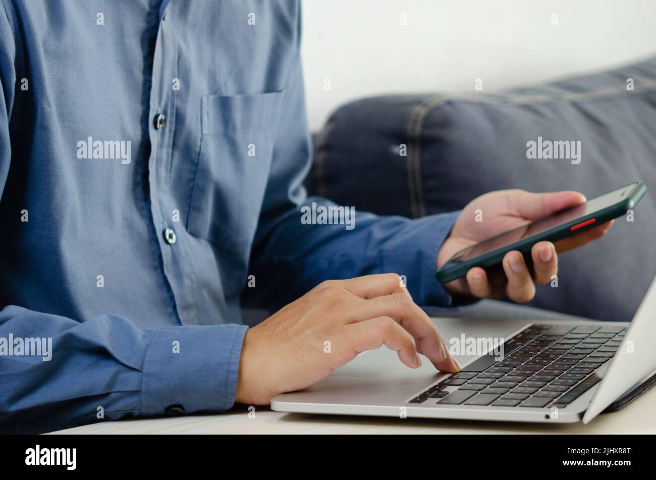 Businessman hand typing keyboard on laptop computer with smart phone. Close up businessman communicating internet and social media at his desk. Stock Photo