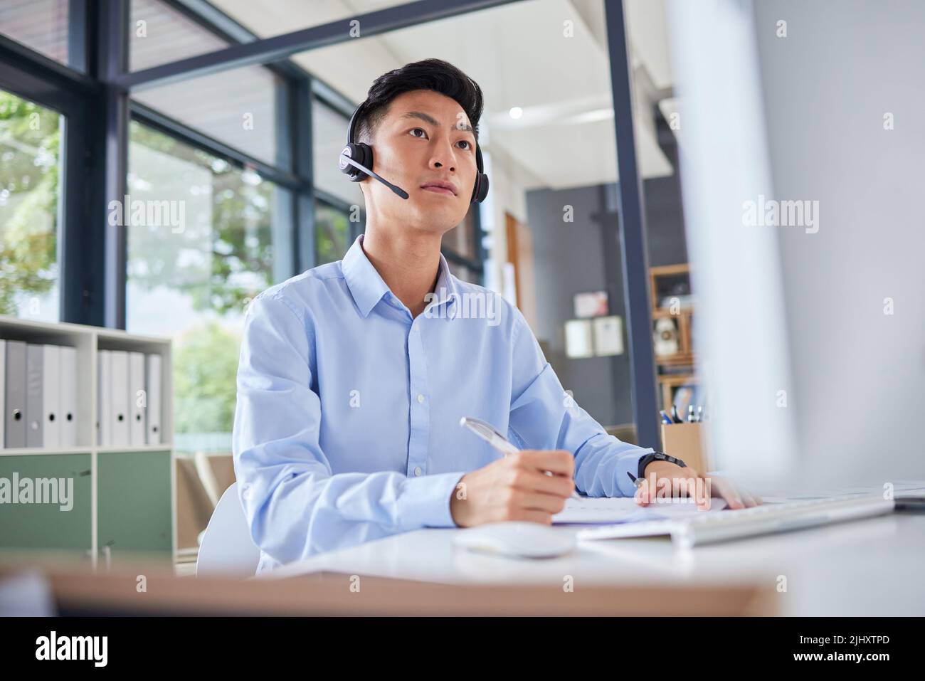 Asian translator or business man with headset looking serious while sitting in office. Accountant checking documents, preparing financial report Stock Photo