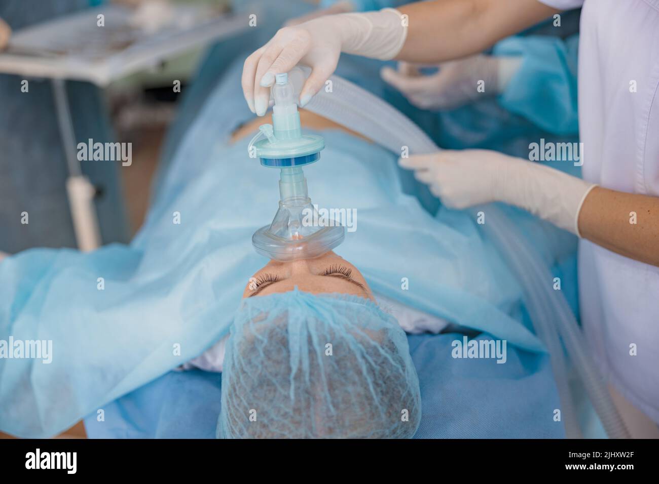 Close up hands of doctor anesthesiologist holding breathing mask on patient face during operation Stock Photo