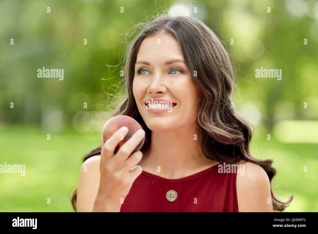 happy woman eating peach at summer park Stock Photo