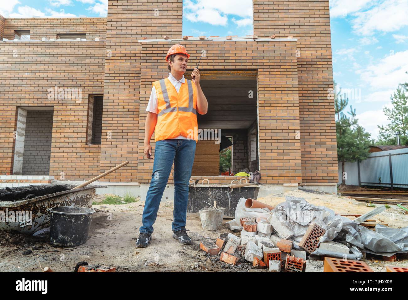 Foreman inspector or construction worker in hardhat portrait. Engineer in helmet with walkie-talkie in hand directs construction process. Stock Photo