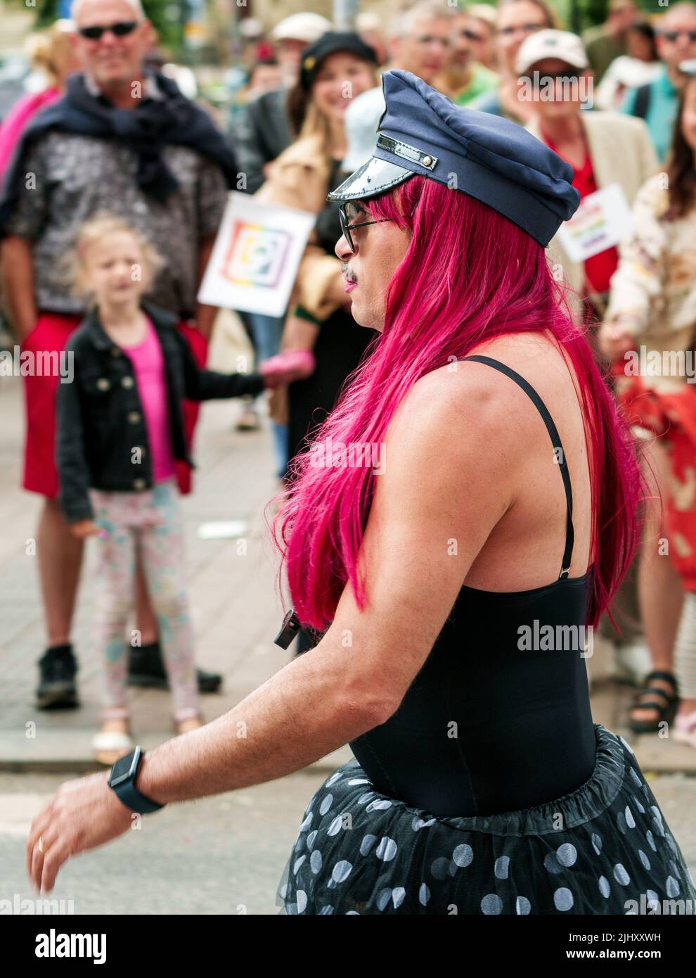 Man in drag walking down the street during Malmo Pride Sweden July 2022. He is wearing a flat cap and has a moustache and long red hair. Stock Photo