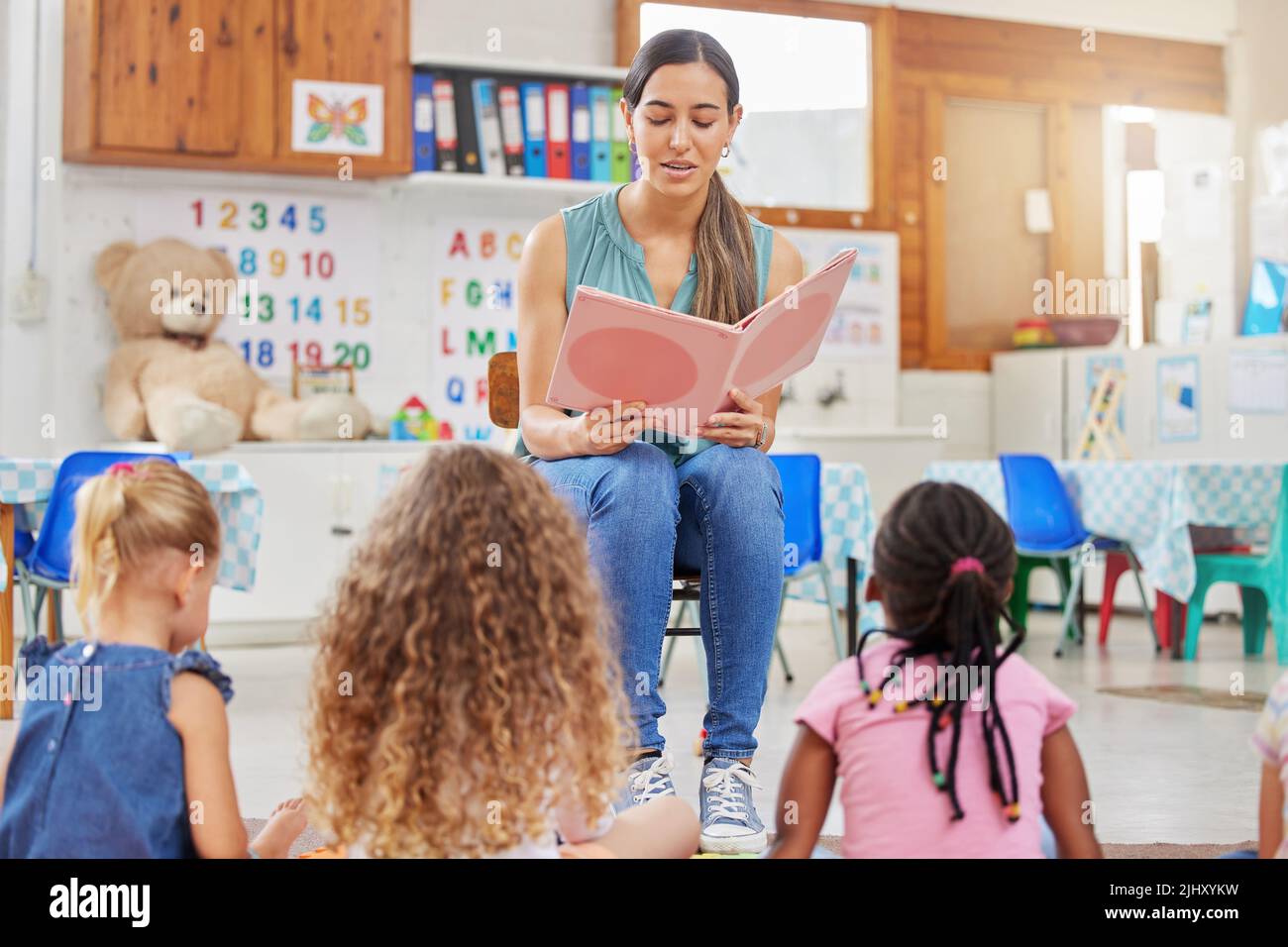 We learn a lot through reading. a young woman reading to her preschool students. Stock Photo