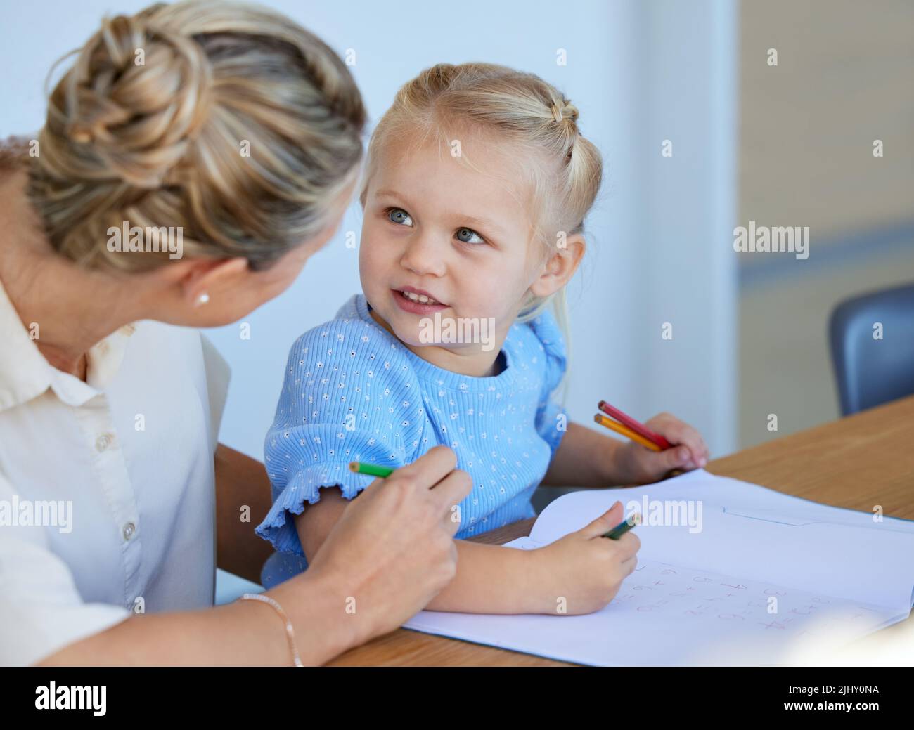 Adorable little girl learning to draw while mother helps her at home