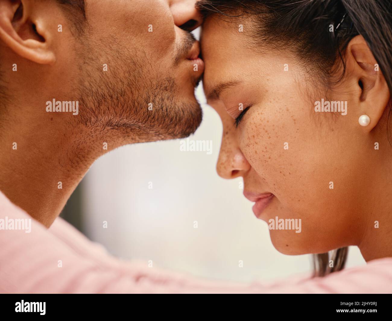 Closeup of mixed race man kissing his girlfriends forehead. Headshot of hispanic couple bonding and sharing an intimate moment at home. Beautiful Stock Photo