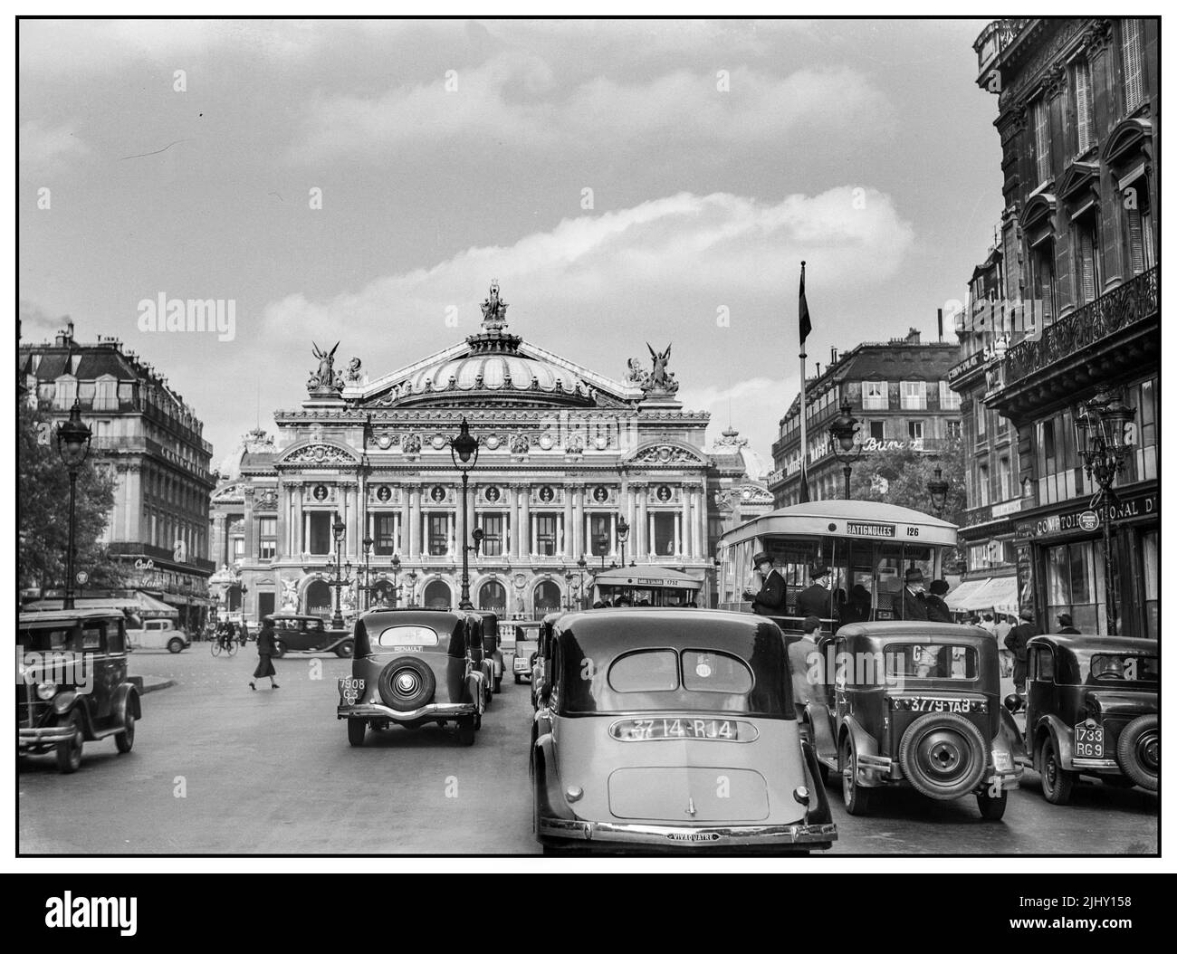 1930s Paris with Renault Taxis on ranks in forground with commuter Autobuses and  L'Opera behind busy with traffic and pedestrians Paris France Stock Photo