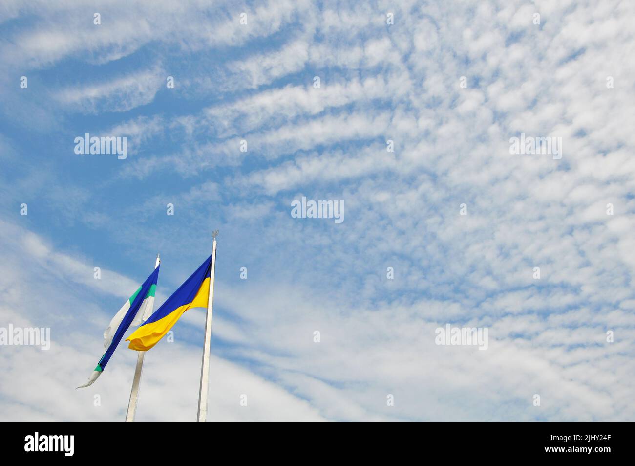 Ukraine bicolor national flag and municipal Rivne city flag waving on the wind against a cloudy sky Stock Photo