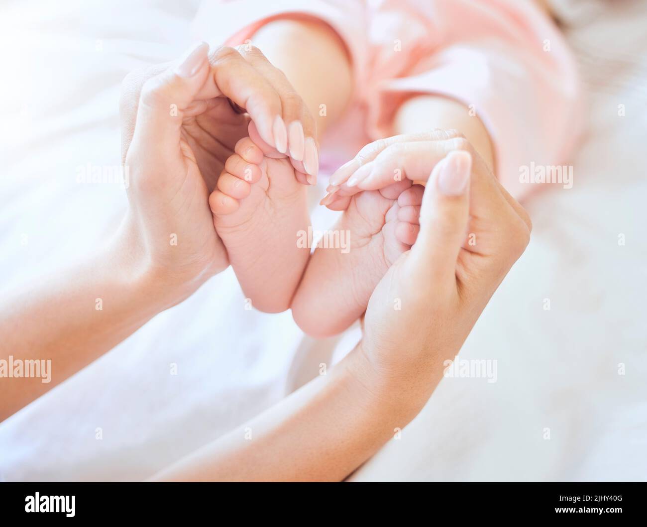 Mother holding baby feet. Closeup of tiny newborn baby feet held by a parent. Small baby toes. Little baby lying on a bed. Woman holding feet of Stock Photo