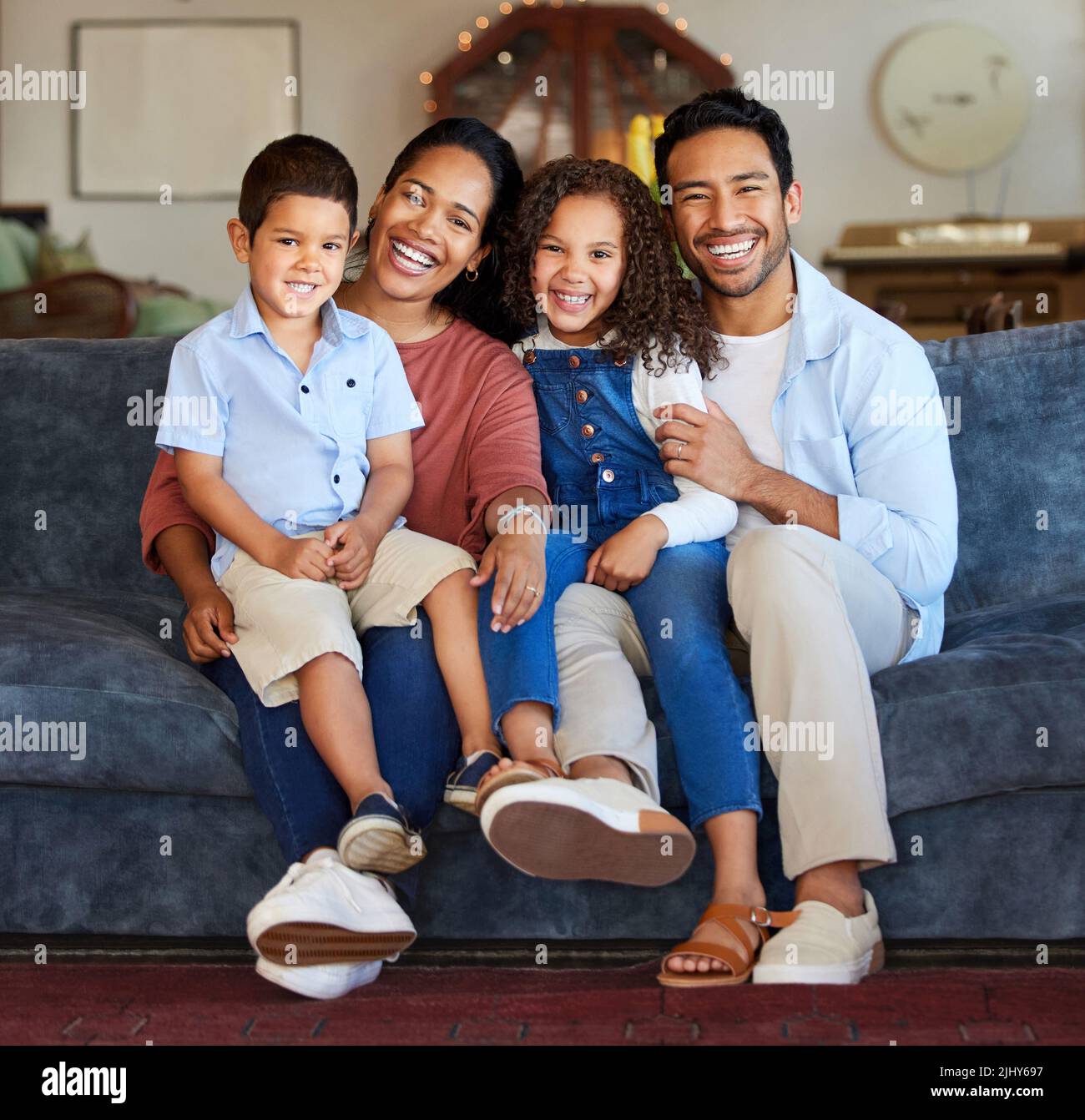 Happy family with two children sitting at home. Happy mixed race family close together on sofa at home. Cheerful mother, father and little children Stock Photo