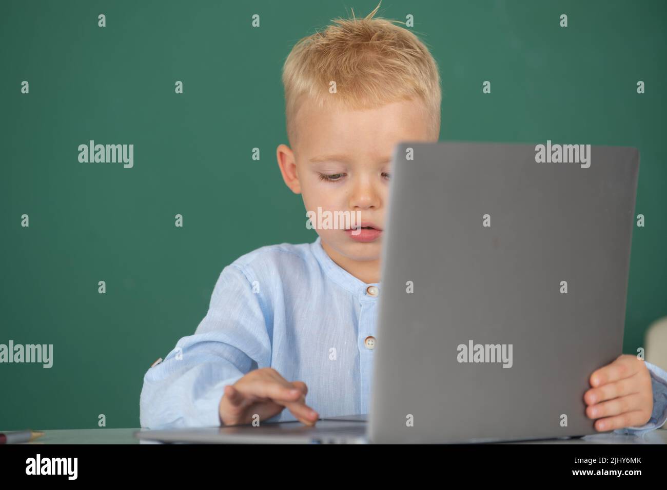 School child using digital pc laptop in class. Portrait of funny pupil of primary school study programming. Cute pupil face closeup on blackboard Stock Photo