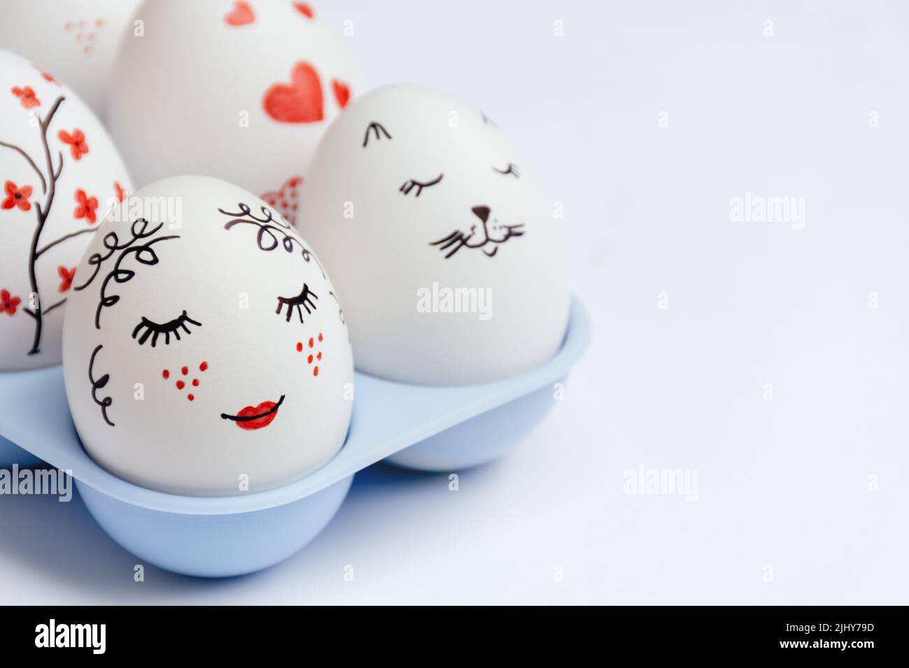 Close up of beautifully painted Easter eggs - gentle beauty with red lips, cat's face, hearts and flowers in blue stand on white background. Handmade master class. Soft Selective focus. Copy Space Stock Photo