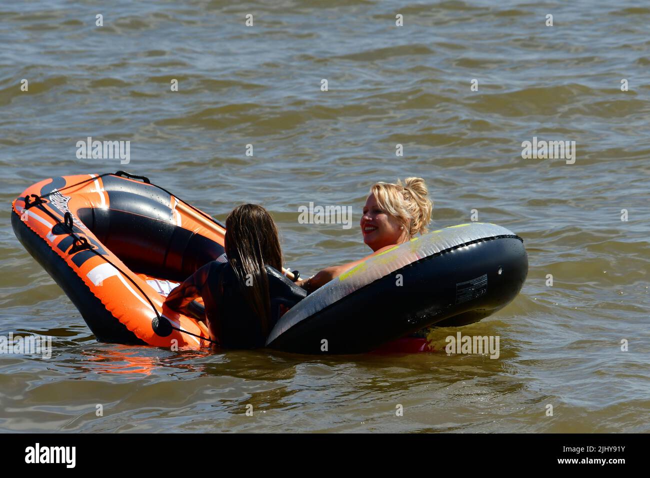 Devon, UK. 21st July 2022. On a very hot and humid afternoon in Sidmouth people are out and about soaking up the afternoon sun in a rubber orange inflatable dinghy Picture Credit: Robert Timoney/Alamy Live News Stock Photo