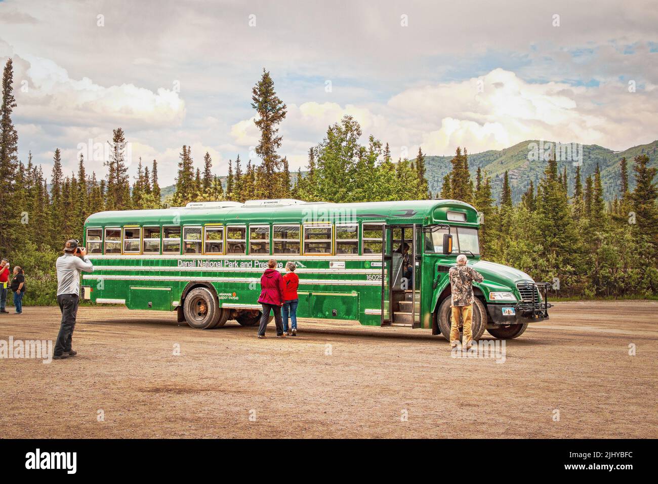 06-22-2002 Denali Alaska USA - Green transit bus in Denali National Park with tourists - one taking a picture - and evergreen trees and mountains in b Stock Photo