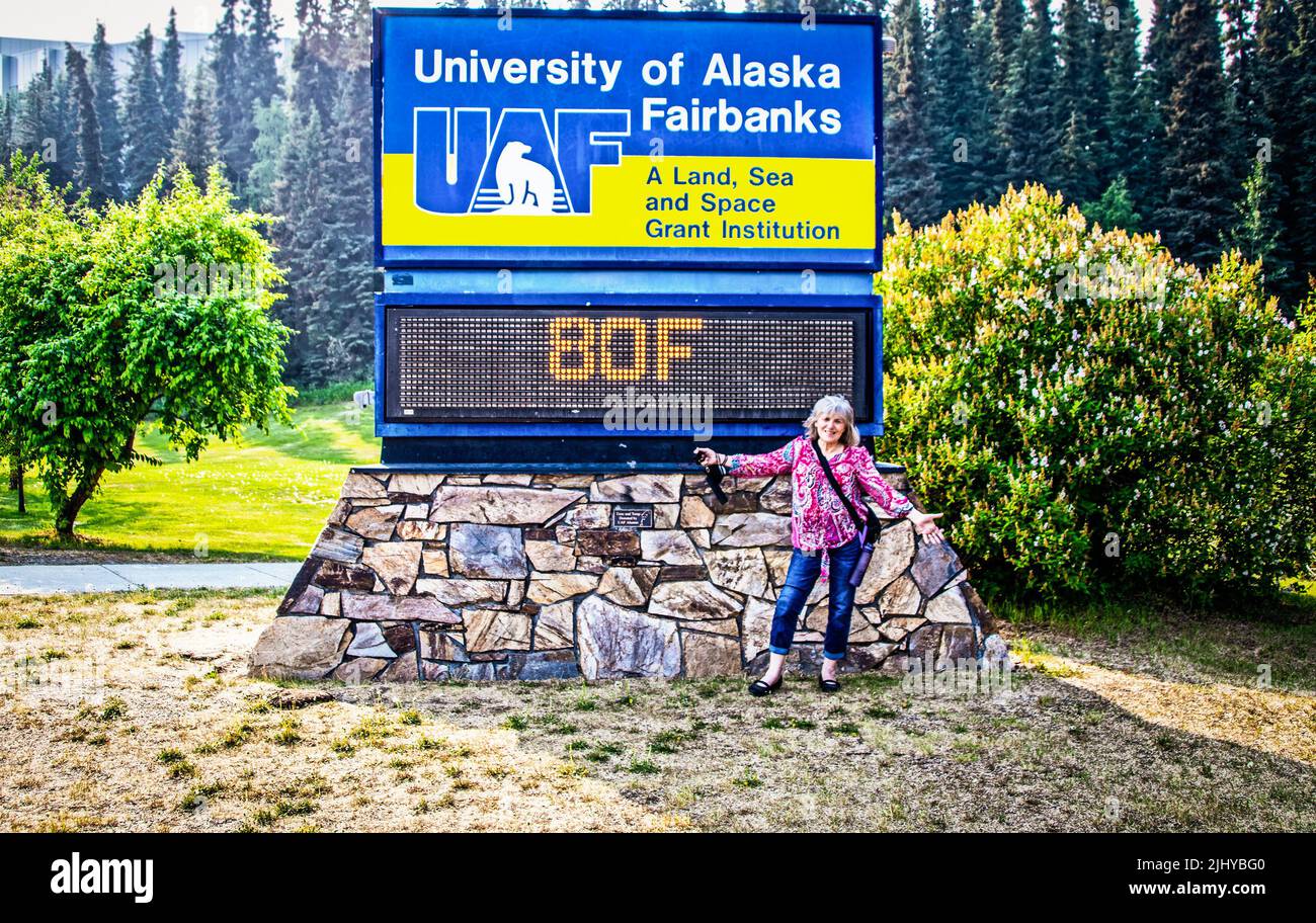 06-27-2022 Fairbanks Alaska USA Woman stading by temperature sign at University of Alaska Fairbanks sign showing unusually hot 80F degrees where stude Stock Photo