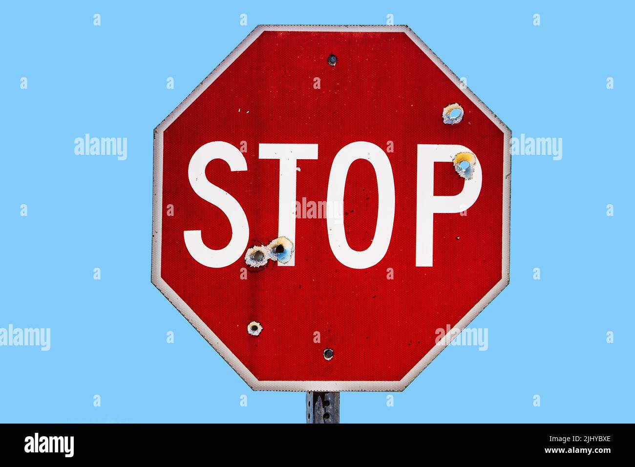 Grungy stop sign shot full of bullet holes isolated on sky blue - room for text Stock Photo