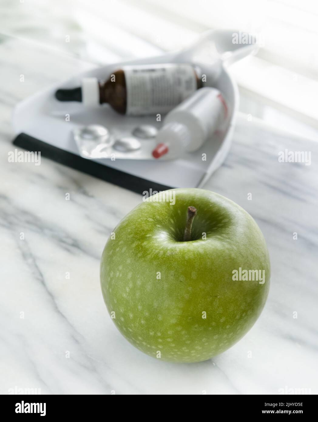 Front, a green apple, background, a dust pan with various medicine containers. Stock Photo
