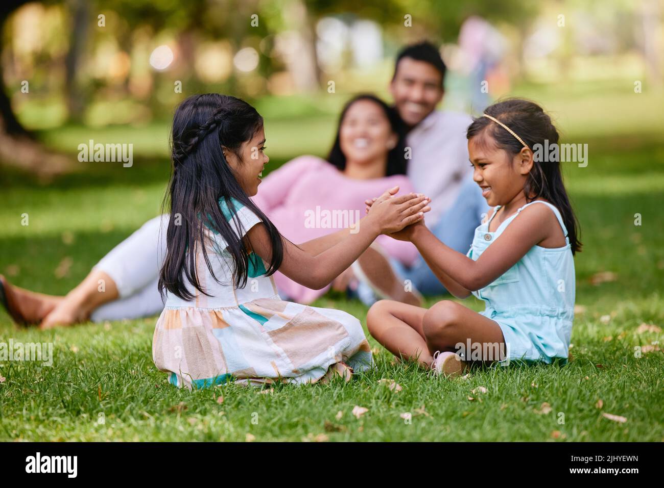 Two little girls playing a clapping game while sitting in the park on a