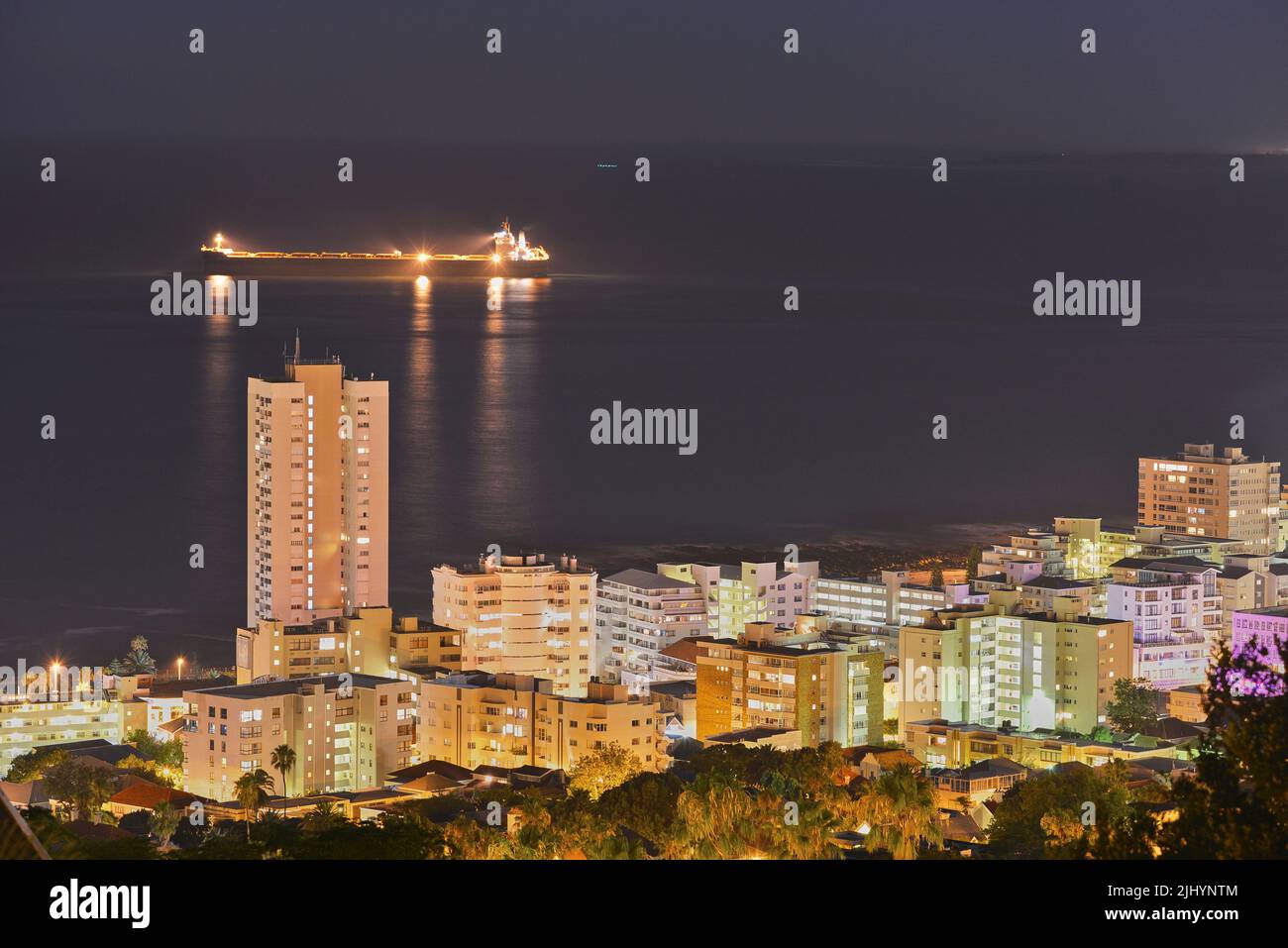 View of skyscraper and city buildings lighting up the dark sky at night, alongside the ocean horizon. Beautiful scenic urban landscape in the evening Stock Photo