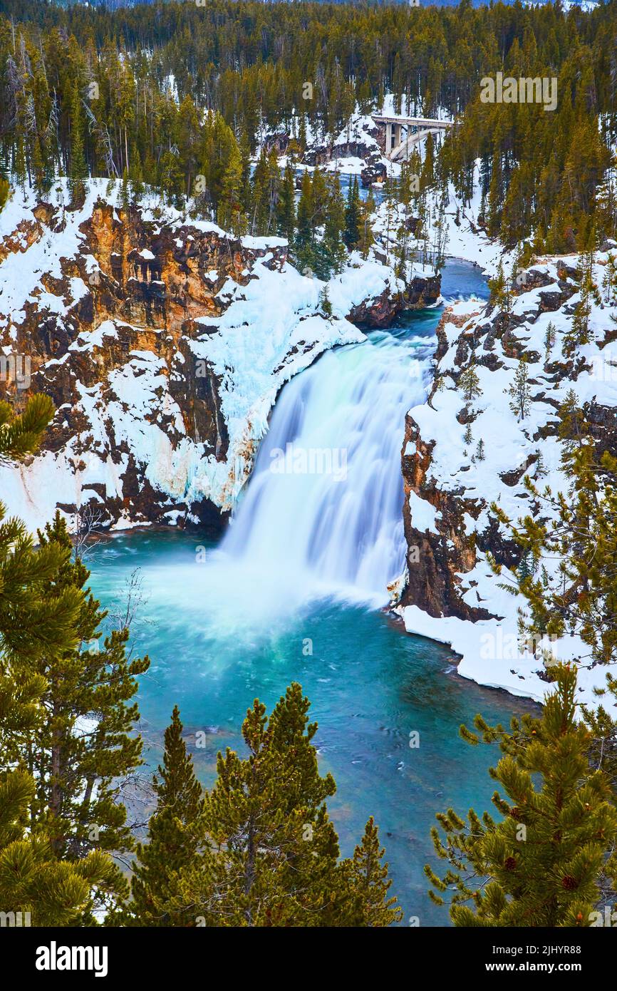 Winter at Yellowstone with snowy cliffs by Lower Falls surrounded in pine trees Stock Photo