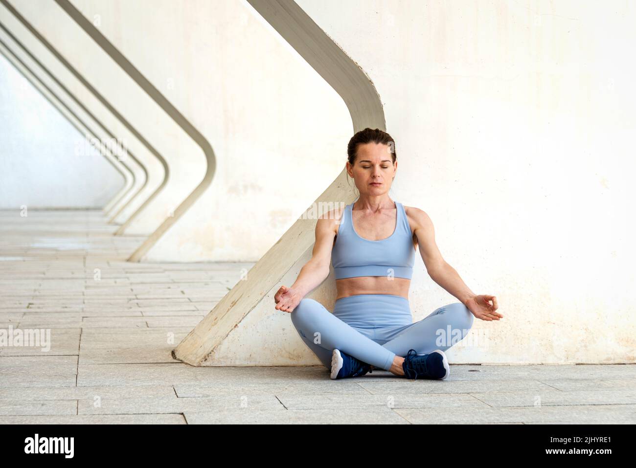 Woman sitting practicing yoga and meditating in an urban setting. Stock Photo