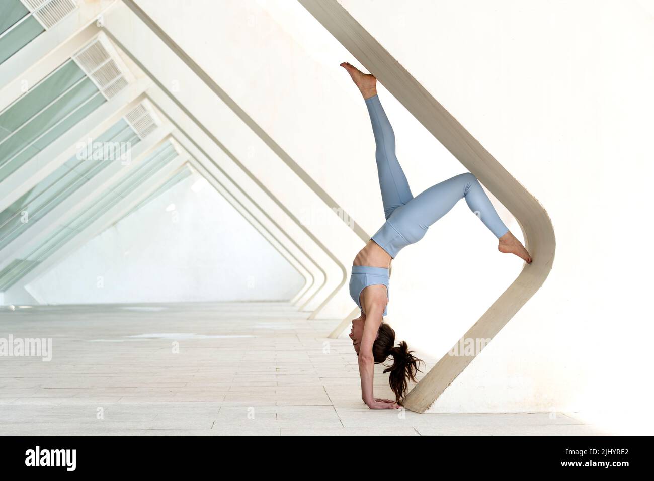 Woman doing a handstand against a concrete arch. Exercise outdoors. Stock Photo