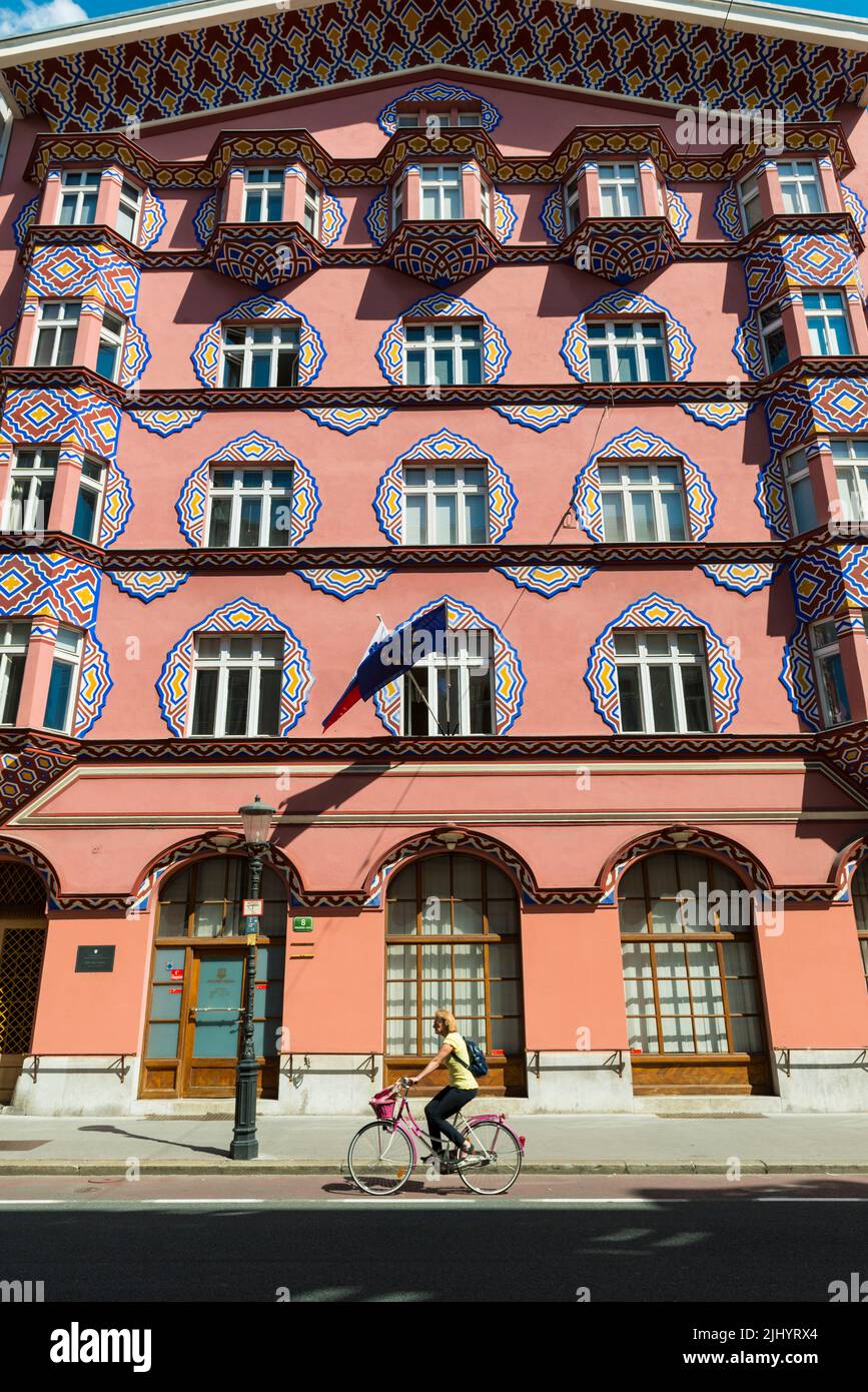Female cyclist passes facade of the Cooperative Business Bank Building designed  by architect Ivan Vurnik and wife Helena Vurnik. Ljubljana, Slovenia. Stock Photo