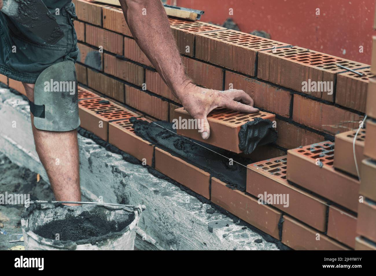 Worker or bricklayer laying bricks. Builder makes brickwork on construction site, close up on hands. Stock Photo