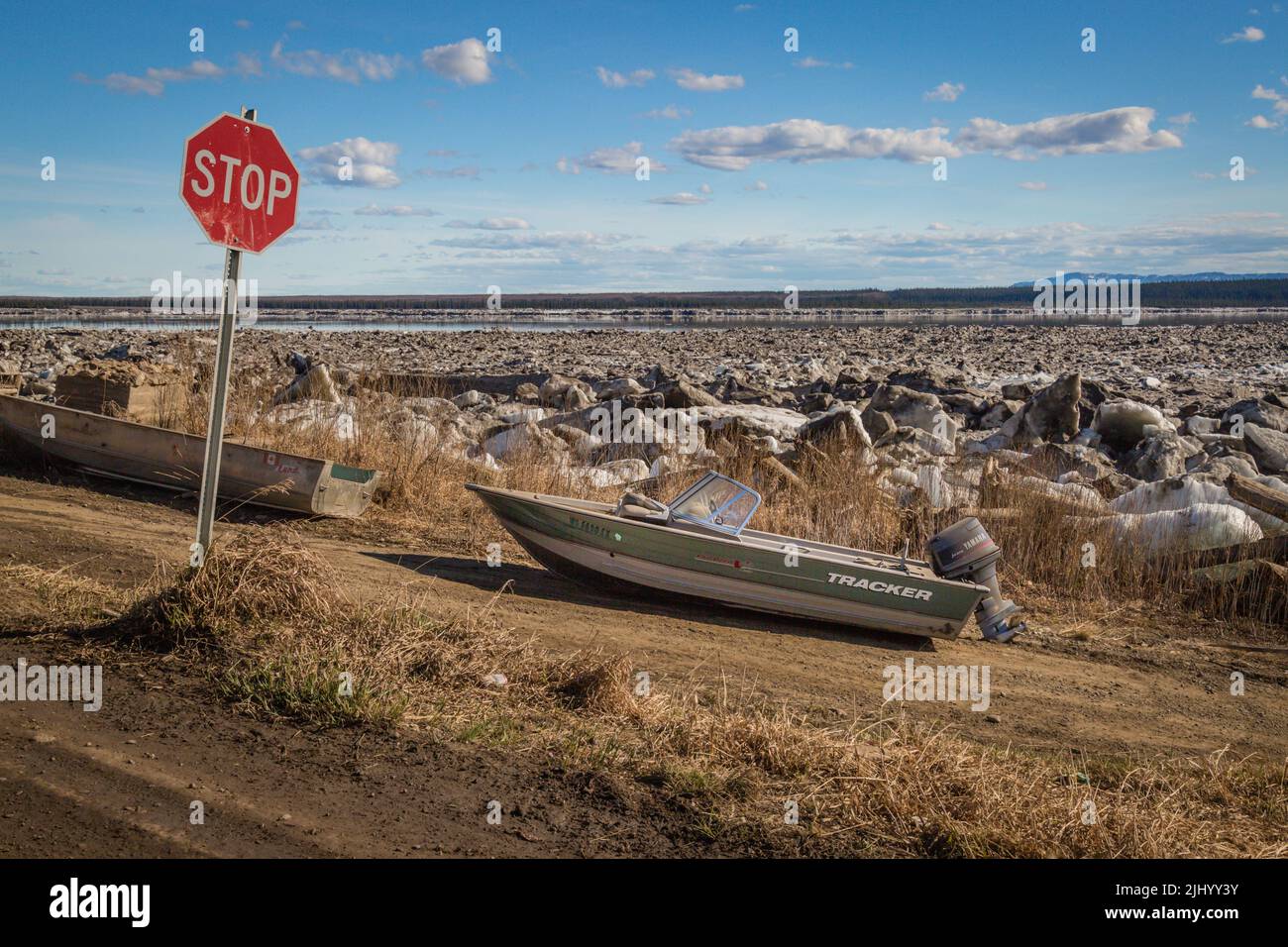 Boat parked on land at stop sign waiting for Great Bear River to thaw in spring, in the Indigenous community of Tulita, Northwest Territories, Canada. Stock Photo