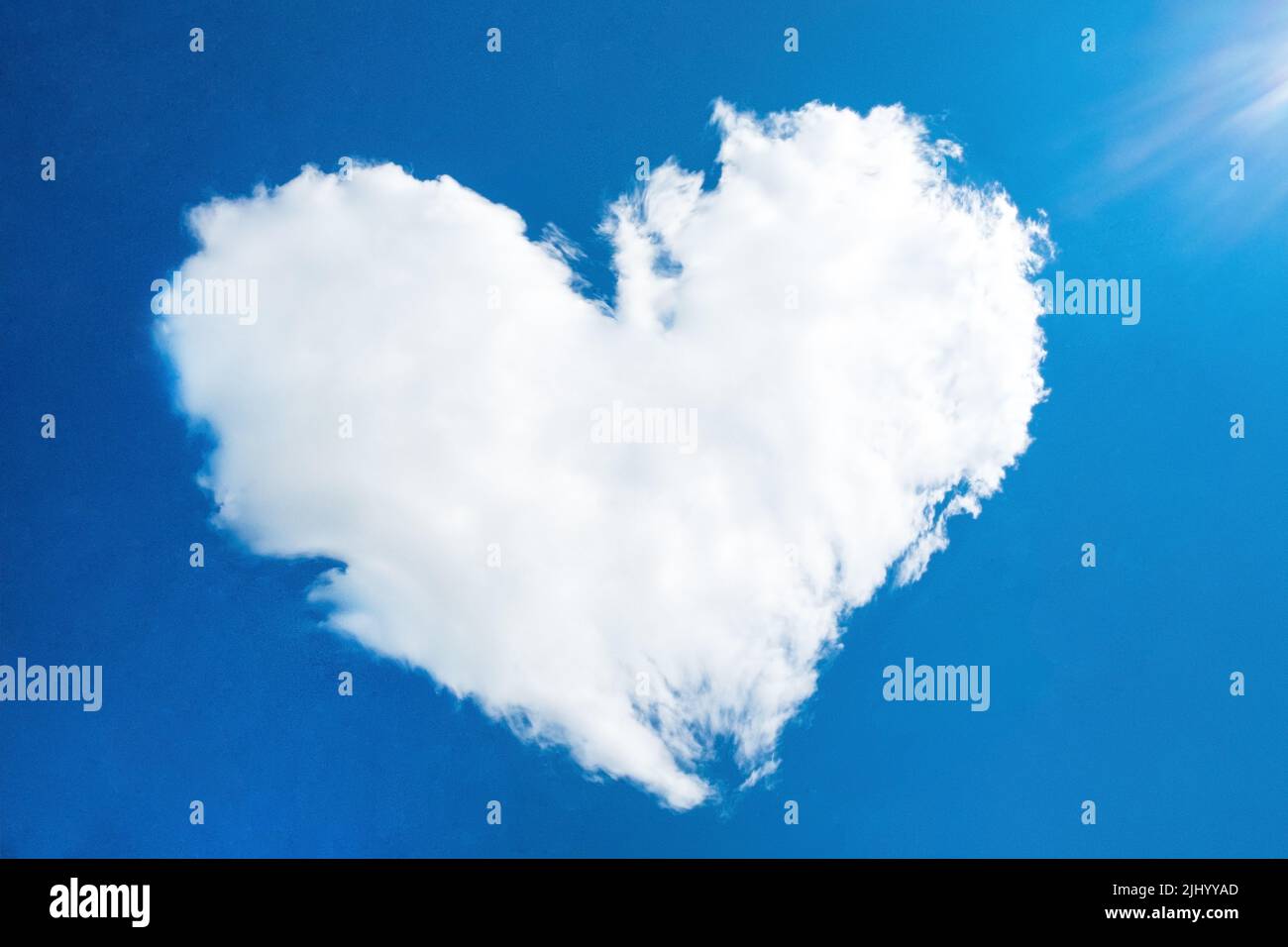 heart in the form of a cloud against the blue sky with the rays of the sun, out of focus. Stock Photo