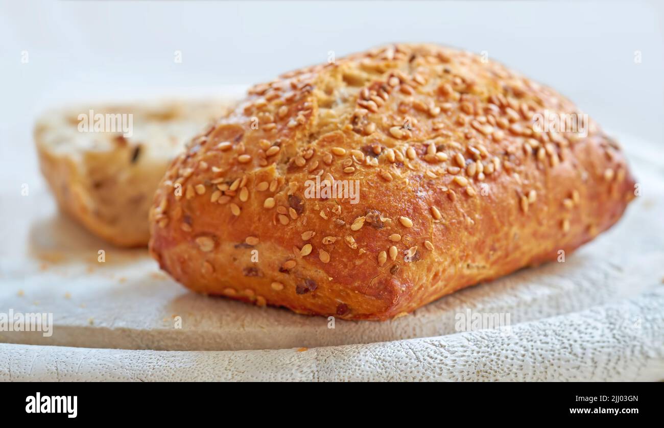 Food stuff. A fresh home baked loaf of wholegrain or wholewheat, sesame seed bread on a board, ready to be cut. For a healthy diet and lifestyle eat Stock Photo