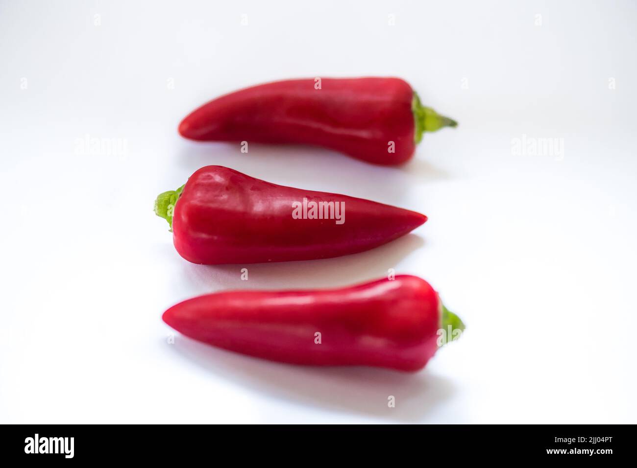 A row of three red peppers on white surface Stock Photo - Alamy